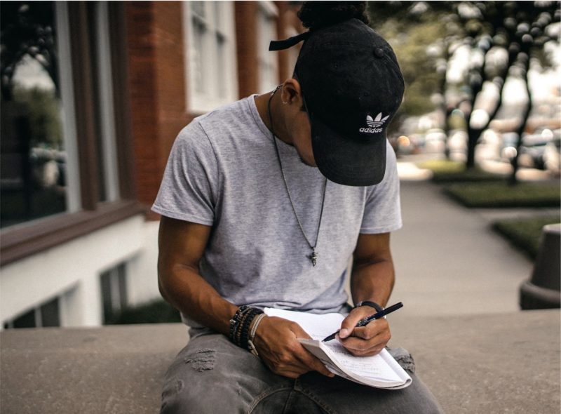 A young man sits outside writing in a notebook