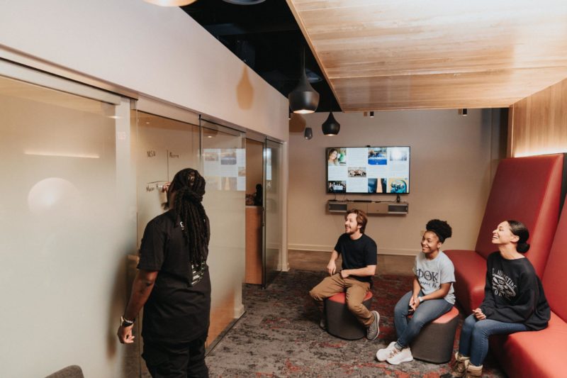 Three students laughing at a whiteboard in a classroom space